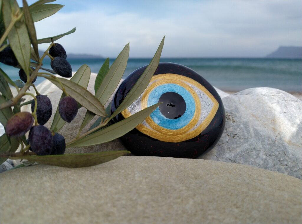 Evil eye painted on rock placed near the sea and olive tree