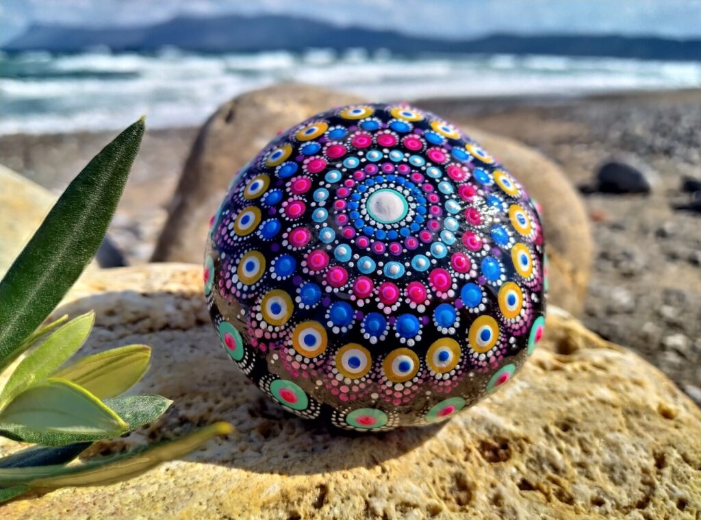 Colorful mandala painted rock by the sea