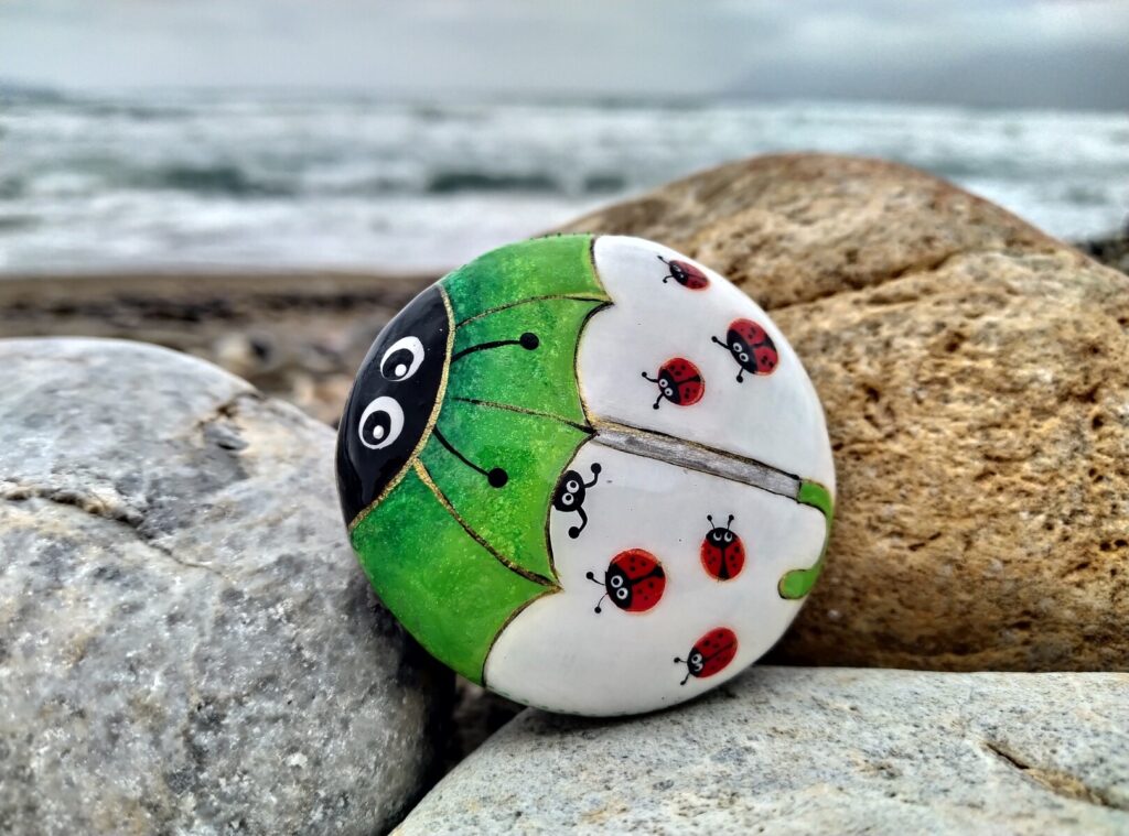 Green ladybug with other small ladybugs painted on stone placed near kissamos beach